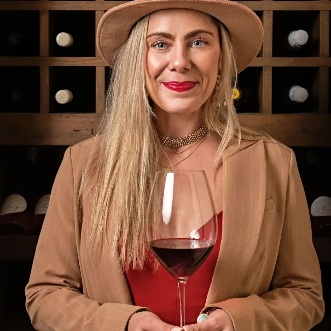 Kristen Carlson with a glass of red wine before a wall of bottles