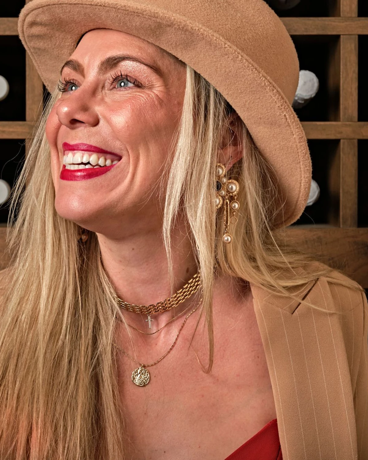 Kristen Carlson laughing with a glass of red wine in front of a wine rack